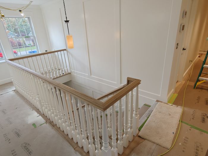 Upper stair landing with white balusters, wood handrail, and paneled walls under finishing.
