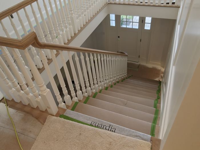 Staircase landing with white balusters, wood handrails, tall windows, and protected stairs.