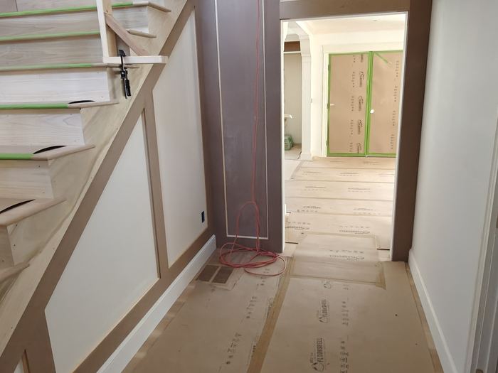 Stair hall under renovation with protected floors and unfinished wood railing.