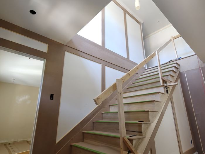Renovated stairwell in progress with paneled walls and unfinished wood railings.