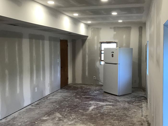 Room with unfinished drywall, recessed lighting, bare floor, and a refrigerator.
